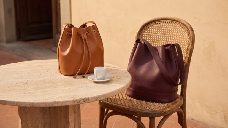 Tan and burgundy Italian leather bucket bags displayed on a stone table and wicker chair at an outdoor café